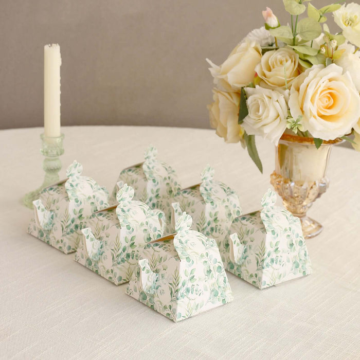 Decorative floral favor boxes arranged on a table with a candle and flowers.
