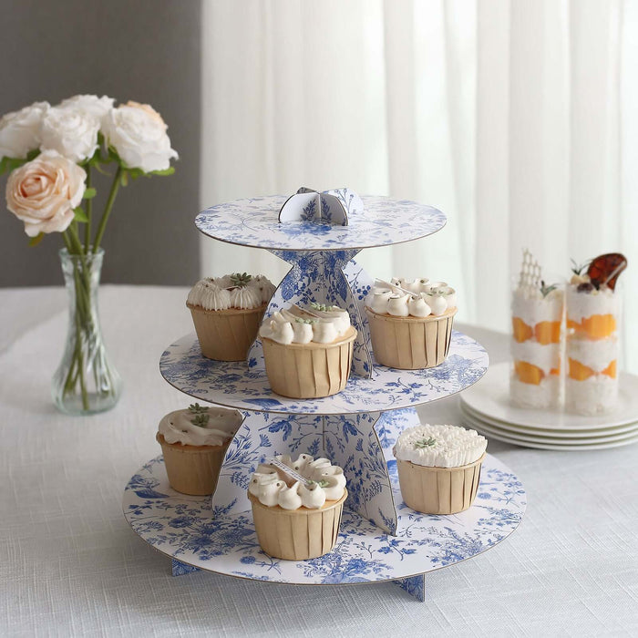 Three-tiered cupcake stand with decorative blue floral design and assorted cupcakes.