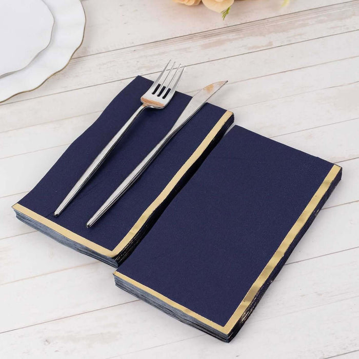 Navy blue napkins with gold trim and silver cutlery on a wooden table.