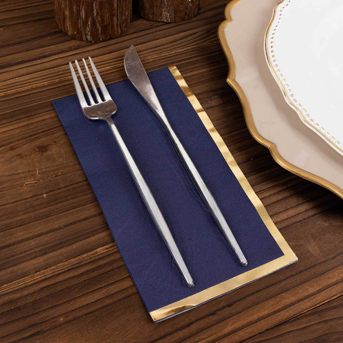 Silver fork and knife on a navy napkin with gold trim, styled on a wooden table.