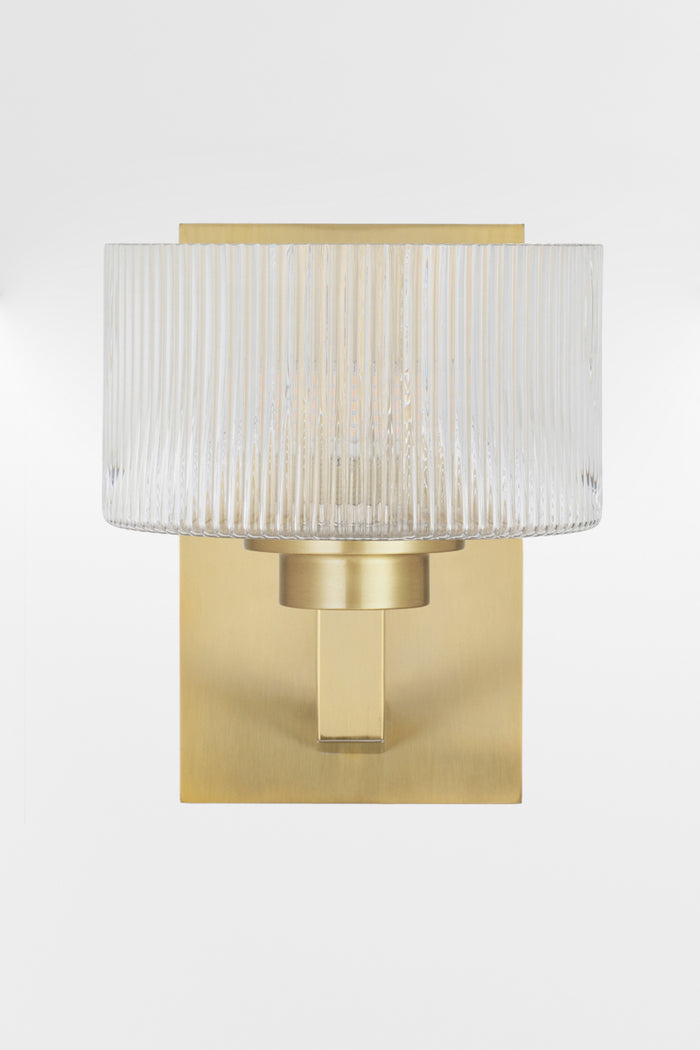 Front view of the wall sconce in Antique Gold with a rectangular mount plate and arm, holding a clear reeded cylindrical glass shade.