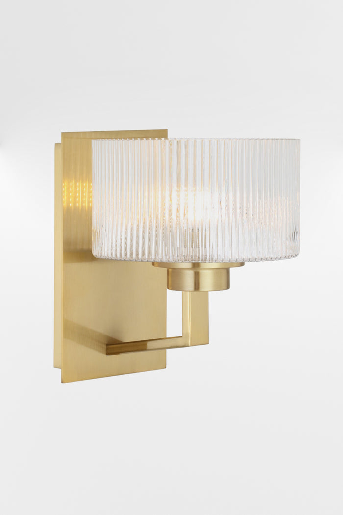 Wall sconce in Antique Gold with a rectangular mount plate and arm, holding a clear reeded cylindrical glass shade.