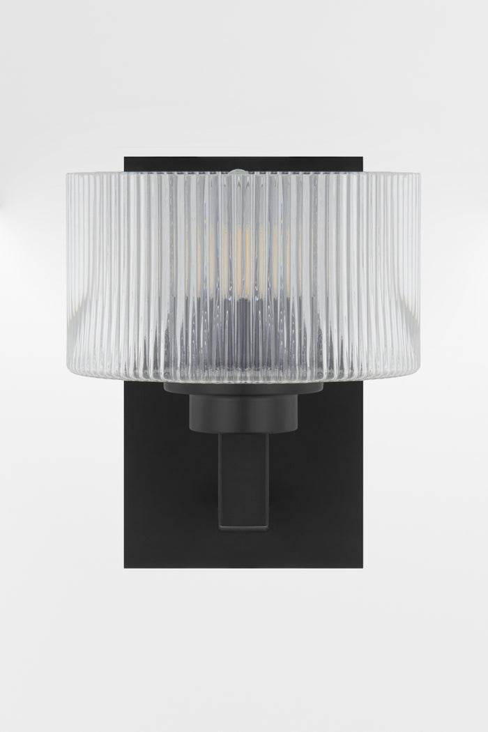Front view of the wall sconce in black with a rectangular mount plate and arm, holding a clear reeded cylindrical glass shade.