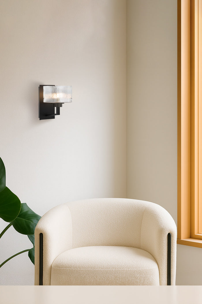 Black wall sconce with reeded glass shade in a bright contemporary sitting space.