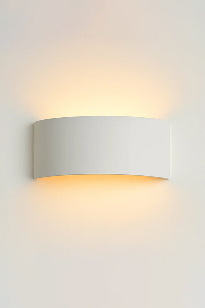 White curved plaster wall light mounted on a white wall, casting a soft warm glow upward and downward.