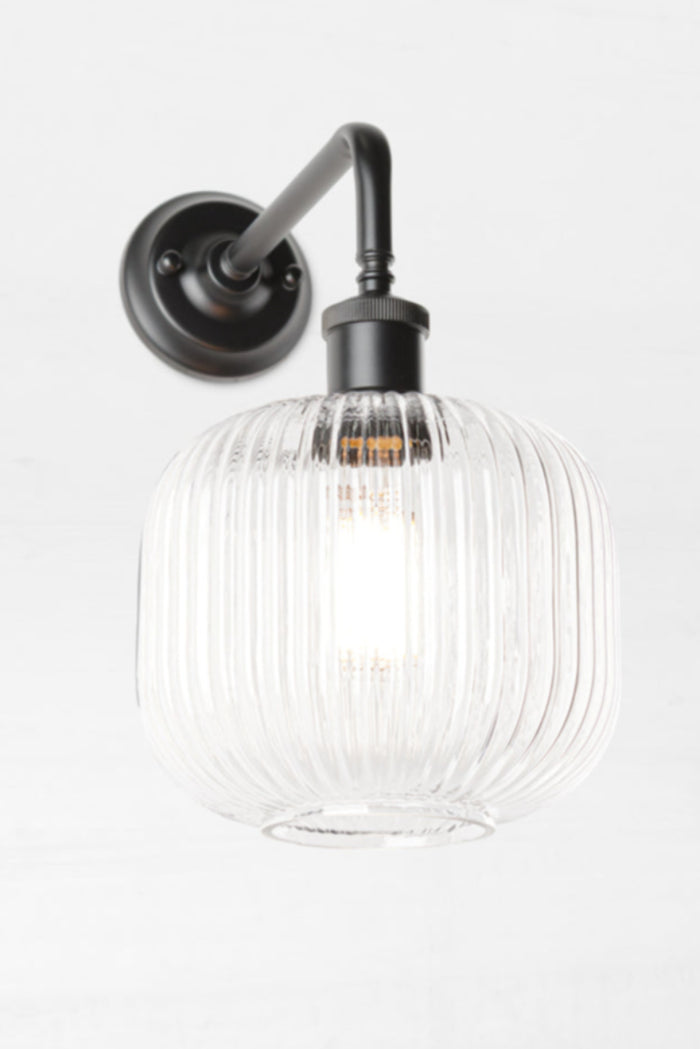 Open clear glass reeded shade paired with a black 90 degree wall sconce.