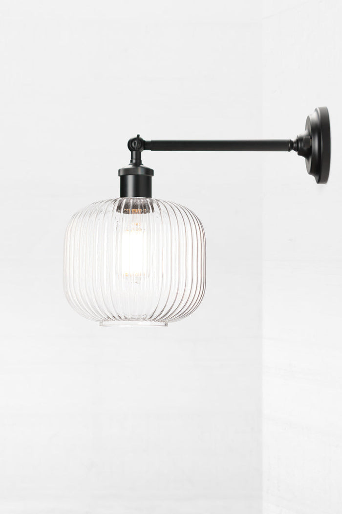 Black swivel wall sconce with long arm and a reeded glass shade in clear.
