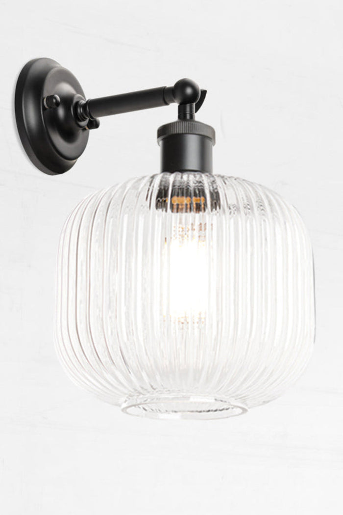 Black swivel wall sconce with short arm and a reeded glass shade in clear.
