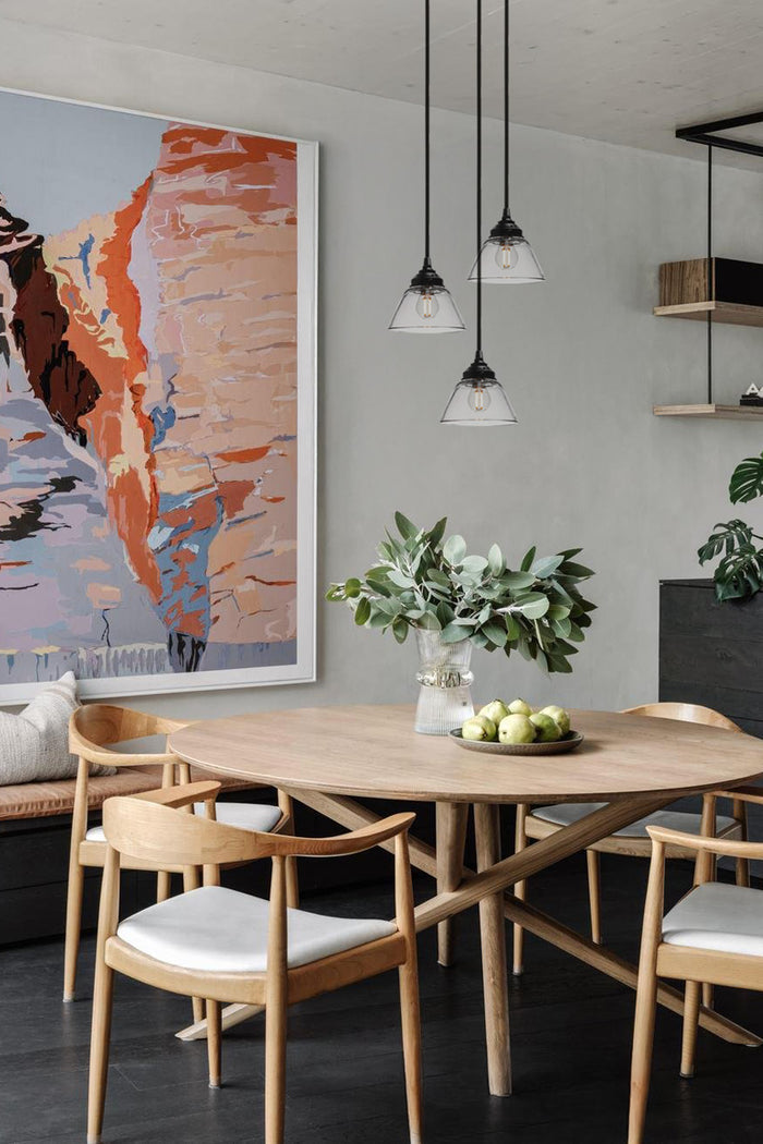 Three clear glass pendant cords with black hardware over a dining space.