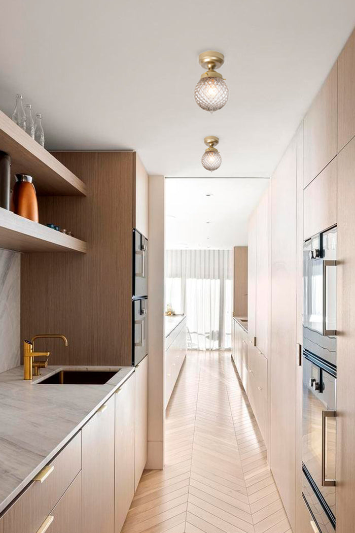 Two detailed clear glass shades on gold/brass batten holders in a light tonal butlers pantry.