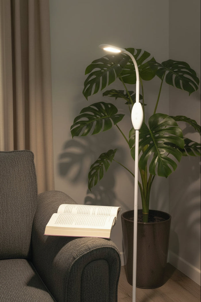 White floor lamp as a reading light next to a couch with an open book and greenery