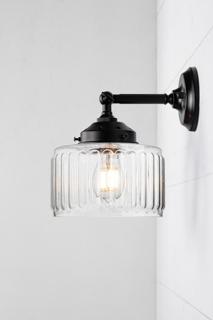 Clear glass shade with vintage fluted detailing on a short, black straight arm wall sconce with a swivel lampholder.