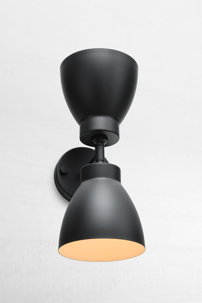 Black double wall sconce with two black metal shades that have a white inner.