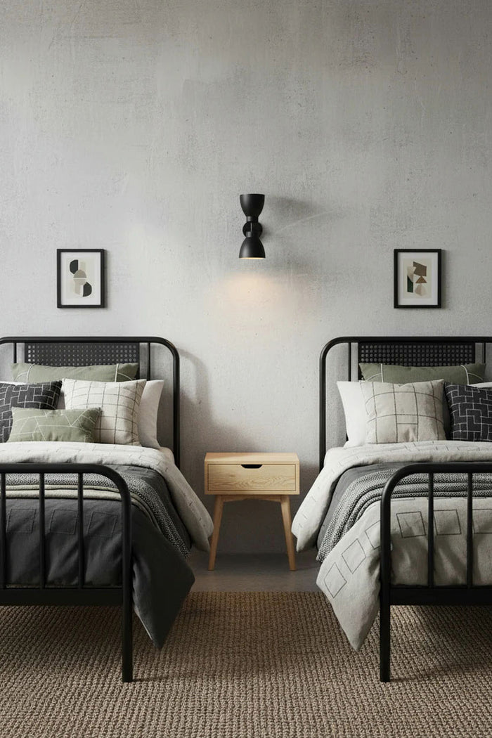 Steel wall sconce has a black finish to complement this urban classic interior bedroom space between two beds.