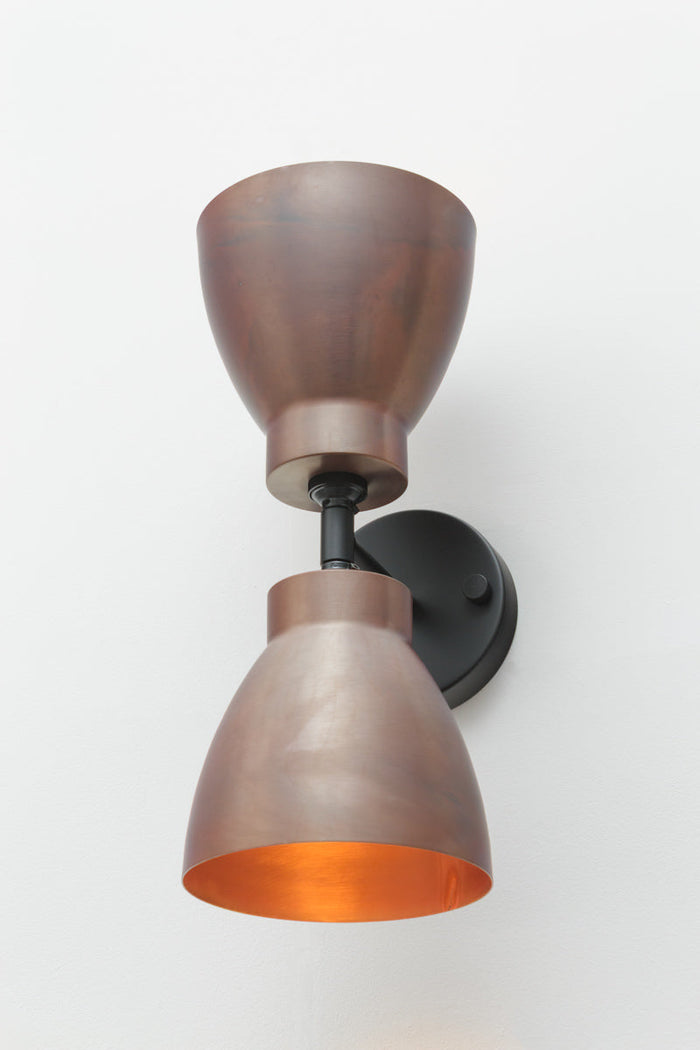 Black double wall sconce with two solid copper bell-shaped shades.