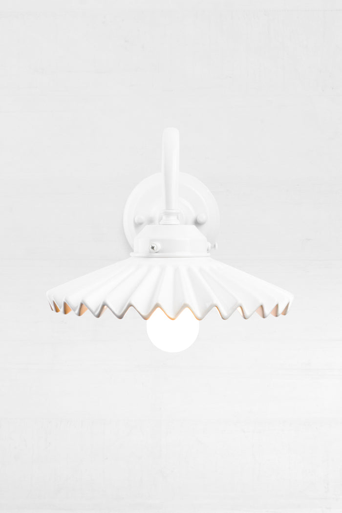 Front view of the white gooseneck wall arm with an integrated 2 and 1/4 cup, paired with a white ceramic shade, showcasing the pleated detail.