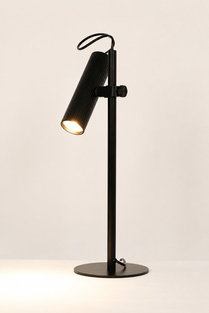 Black Collie desk lamp with the light on in a white space.