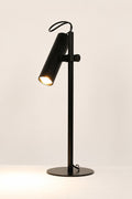 Black Collie desk lamp with the light on in a white space.
