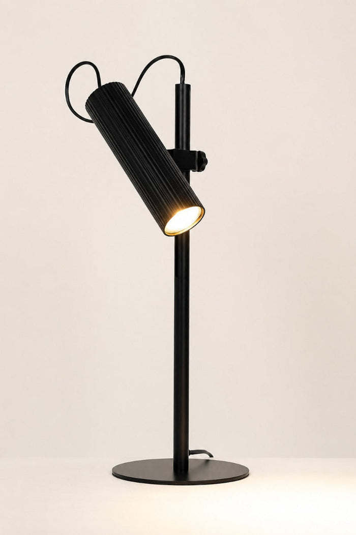 Tilted angle of the Black Collie desk lamp with the light on in a white space.