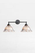 Black double swivel wall sconce with large clear glass shades with reeded detailing and a frilled edge