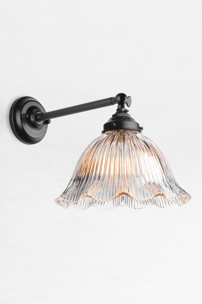 Long arm wall sconce in black with a clear holophane shade with a frilled edge.