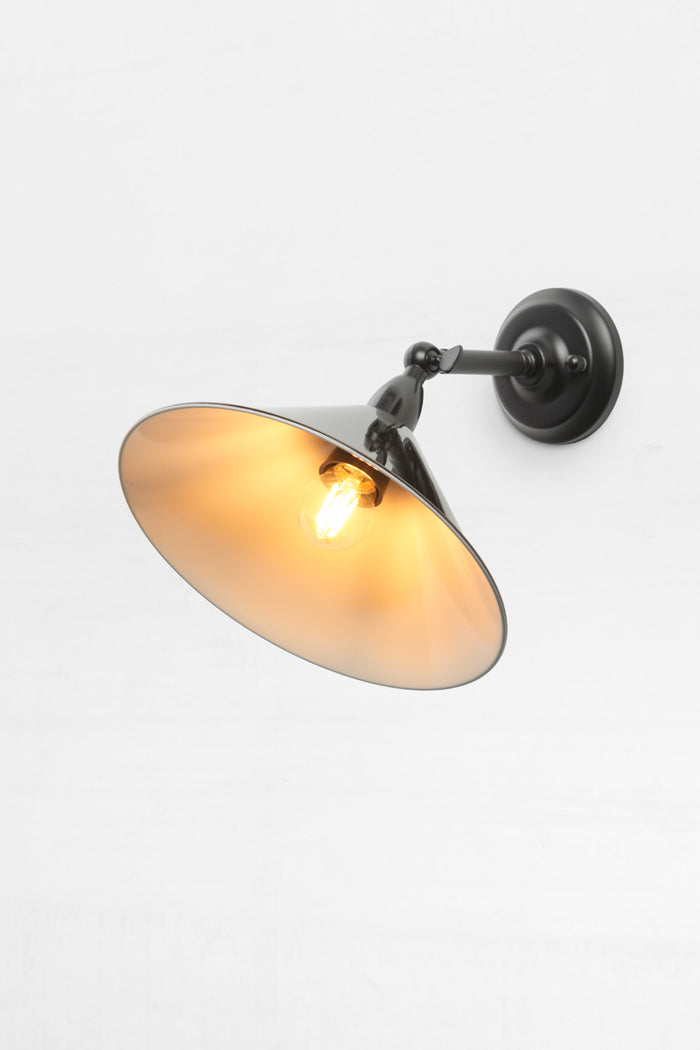 Small metal cone shade in black with short straight arm outdoor wall sconce showcasing the swivel lampholder and white shade inner.