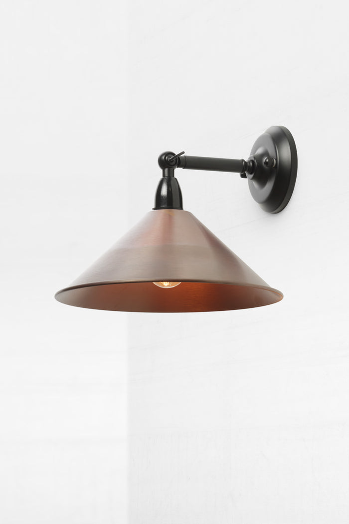 Small metal cone shade in aged copper on short straight arm, outdoor wall sconce with swivel lampholder.