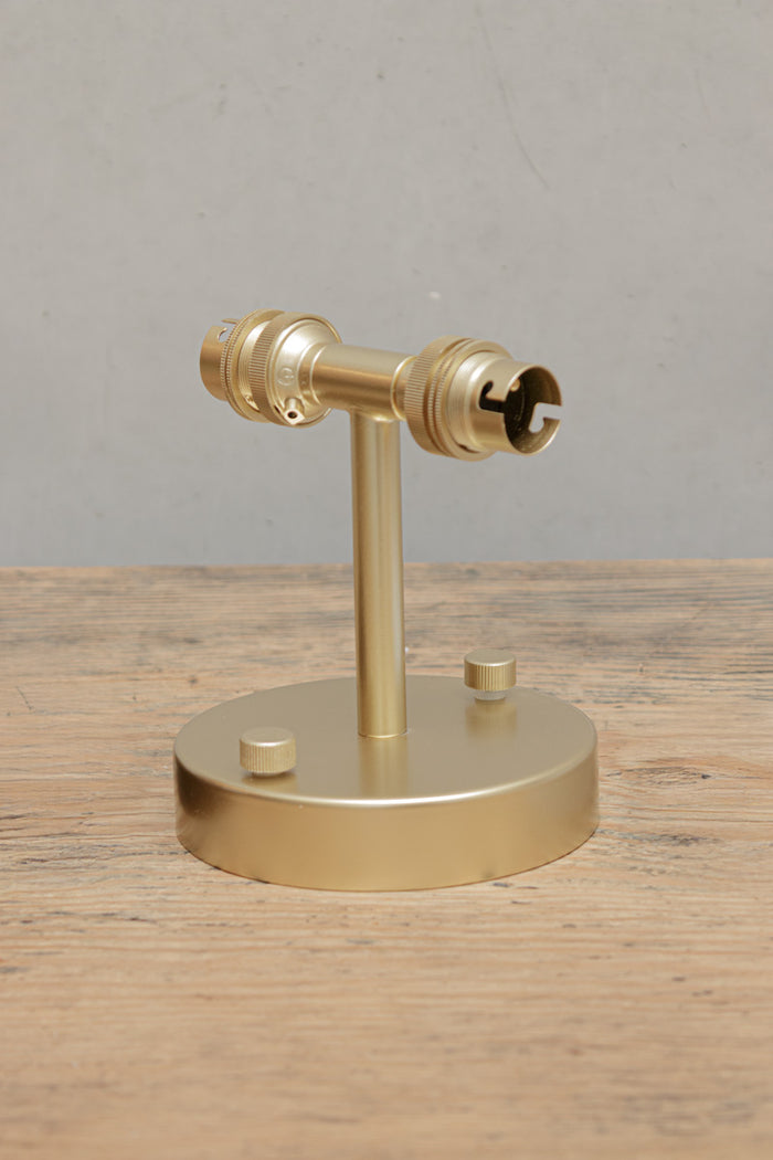 Gold/brass double wall sconce, uninstalled sitting on a timber bench.