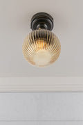 Under view of an amber reeded glass ball shade on a black flush mount that is IP rated.