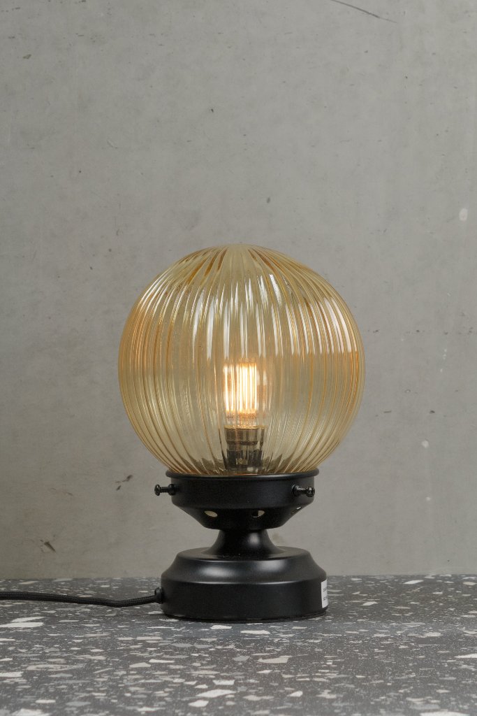 Amber reeded glass ball lamp with a black base.