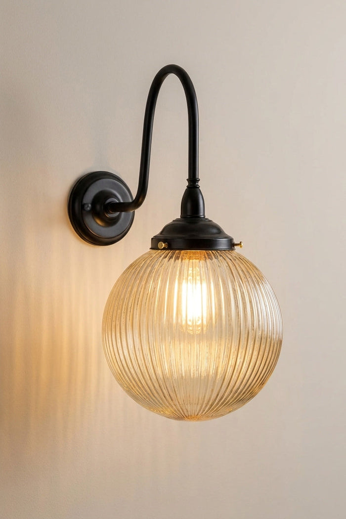 Illuminated medium amber reeded glass ball shade on an extra large gooseneck outdoor wall arm in black.