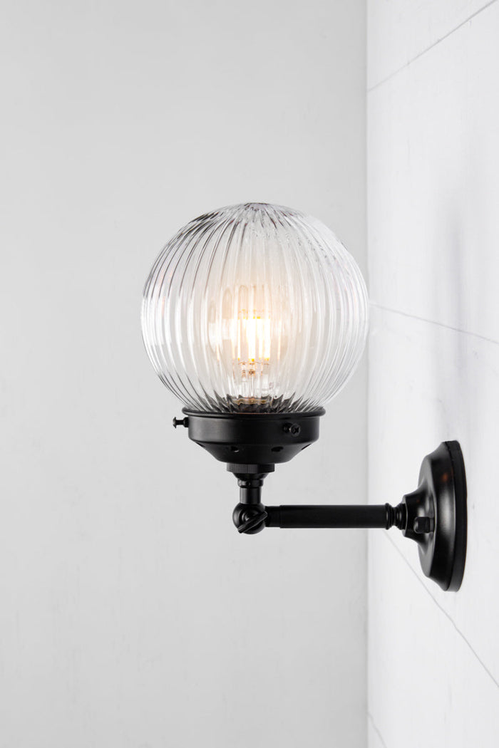 Side view of clear glass reeded ball shade on a short black swivel straight arm.