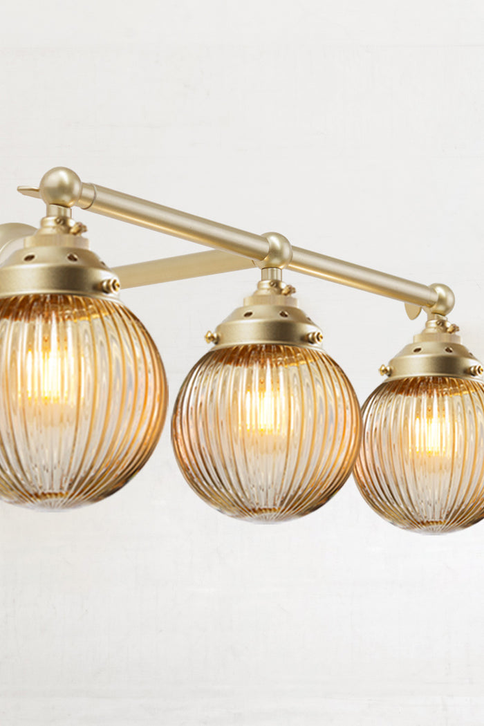 Triple straight arm wall sconce in gold/brass with amber reeded glass ball shades- close up view.