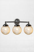 Triple straight arm wall sconce in black woth amber reeded glass ball shades- front view.