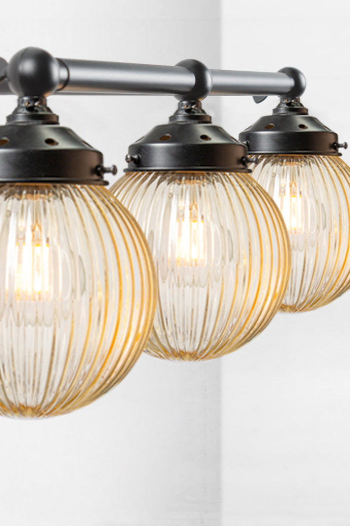 Triple straight arm wall sconce in black woth amber reeded glass ball shades- close up view.