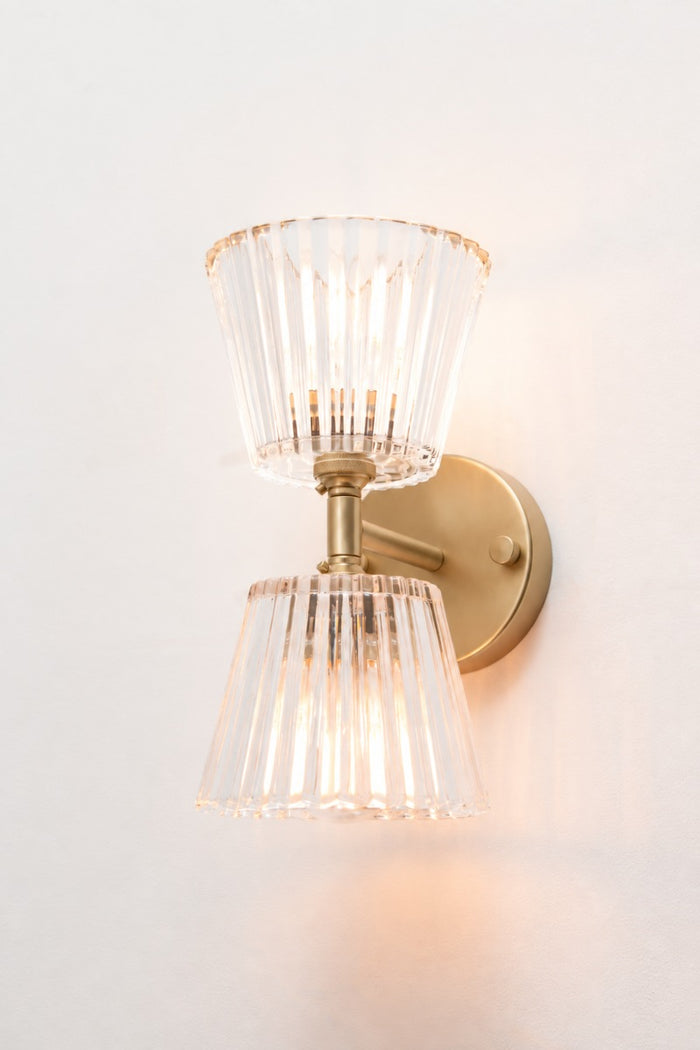 Angled view of gold/brass Davis Glass Double Light Wall Sconce with two illuminated clear glass shades