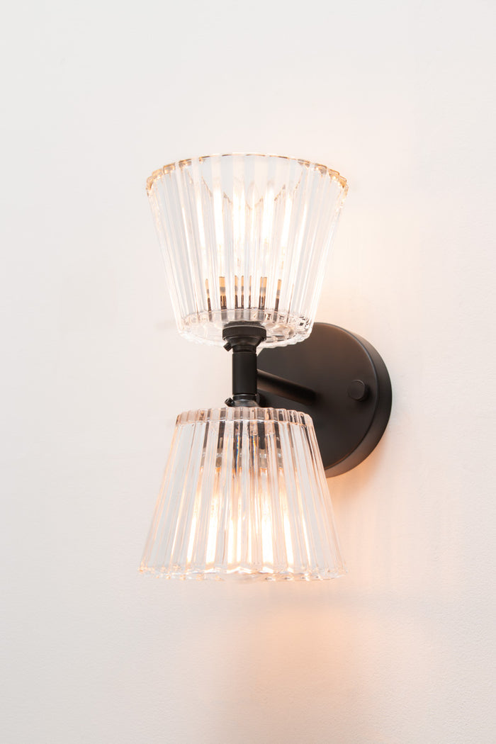 Angled view of black Davis Glass Double Light Wall Sconce with two illuminated clear glass shades