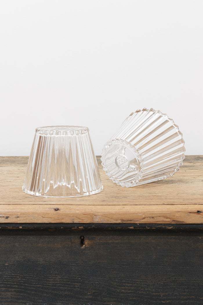 Clear fluted glass shades displayed on a rustic timber surface, showcasing the tapered silhouette and vertical ribbed detailing.