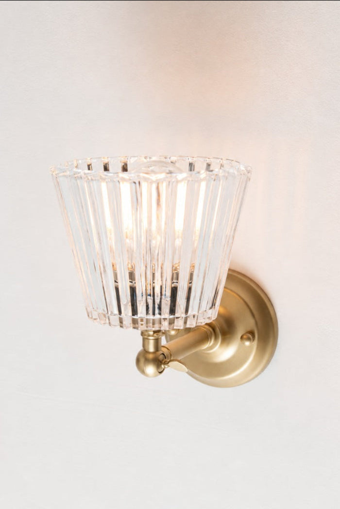 Davis Glass Swivel Arm Wall Light, with a gold/brass arm, illuminated against a light wall