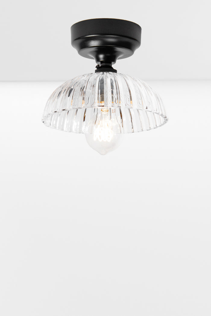 Black batten holder paired with a clear glass shade with deep fluting and a scalloped edge.