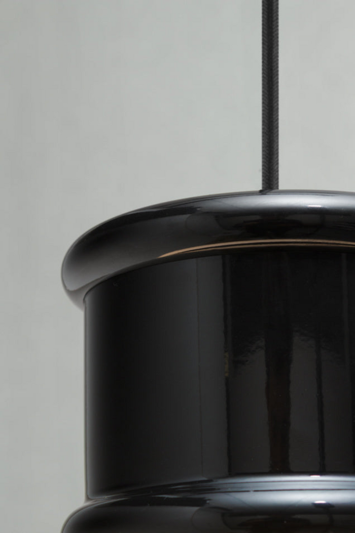 Close-up of a glossy black cylindrical pendant light fixture with a matching black hanging cord