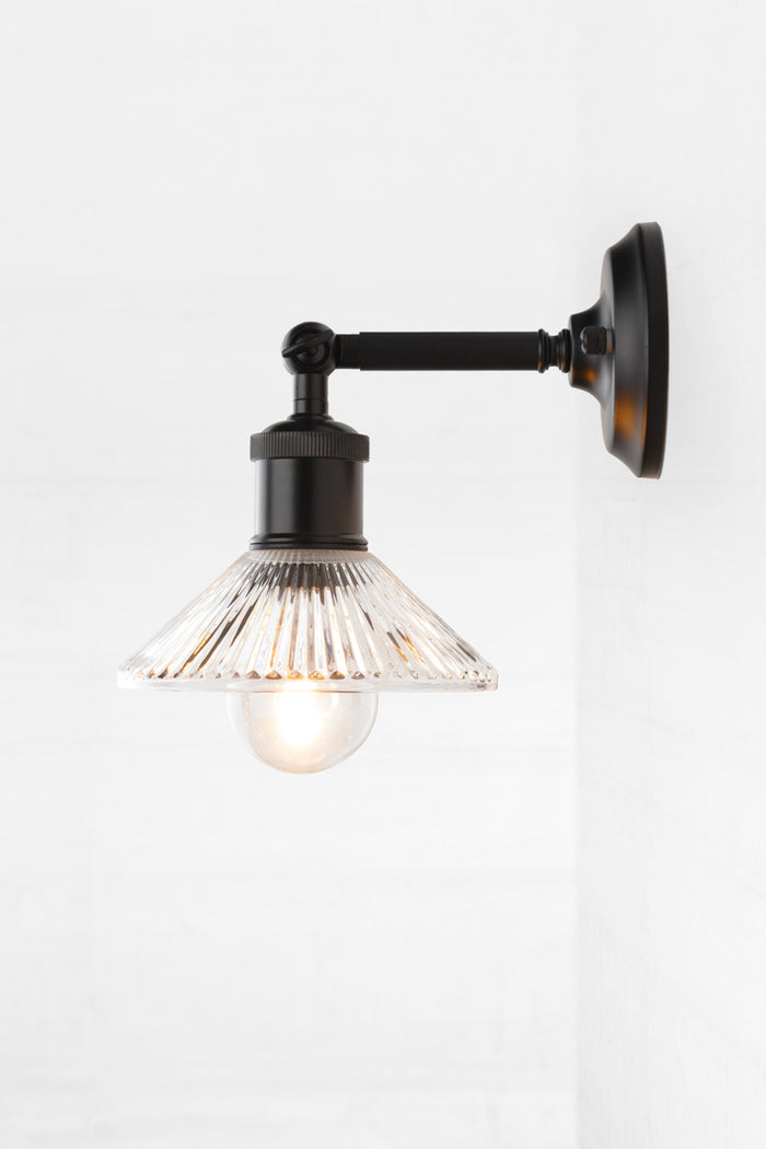 Side view of the pleated clear glass shade with clear bulb on a short, black outdoor wall sconce.