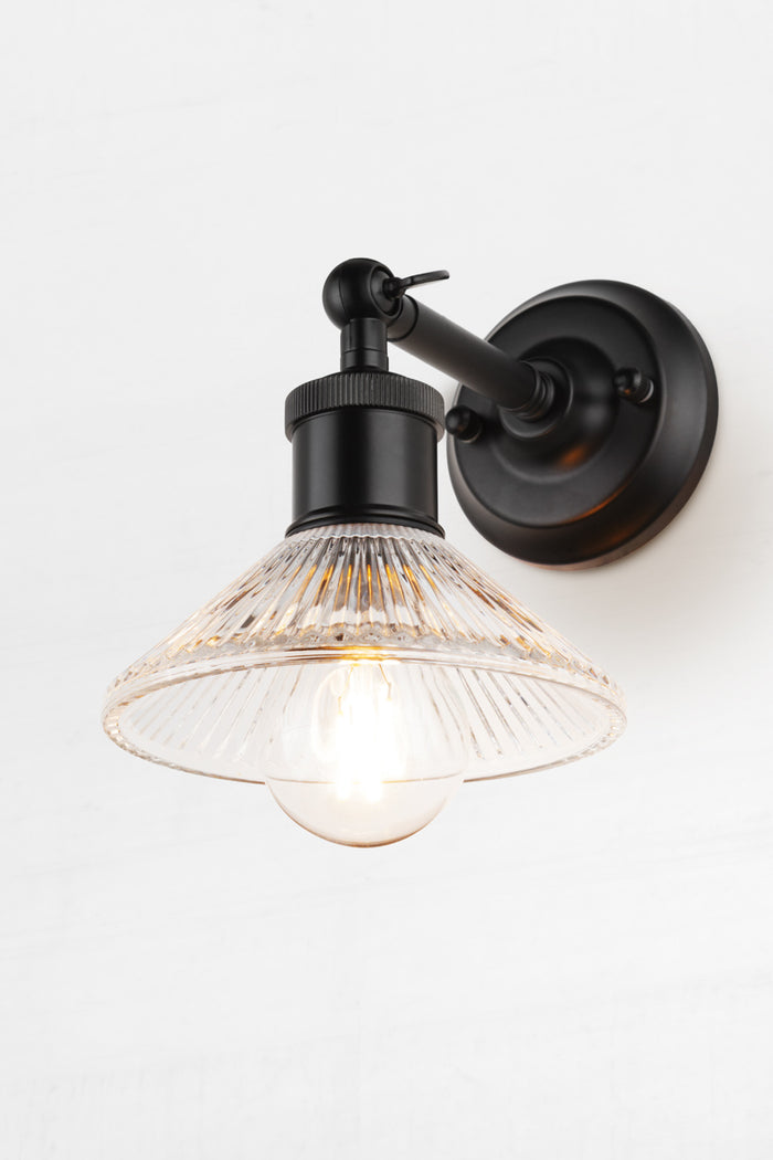 Pleated clear glass shade with clear bulb on a short, black outdoor wall sconce.