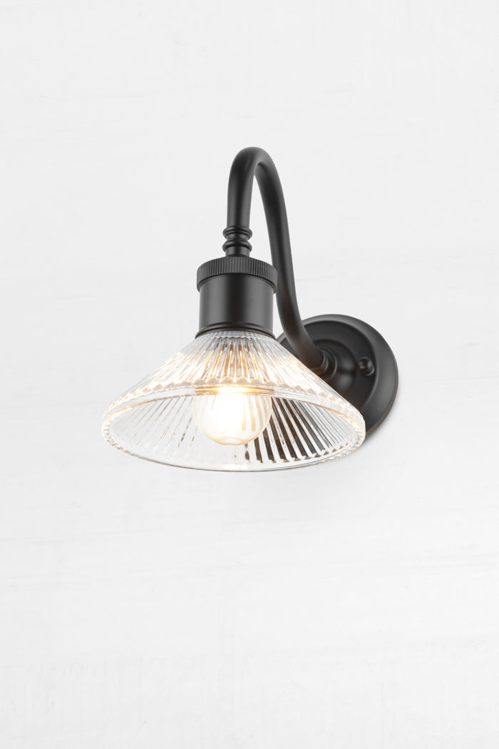 Angled view of the clear pleate glass shade on the black gooseneck outdoor wall sconce.