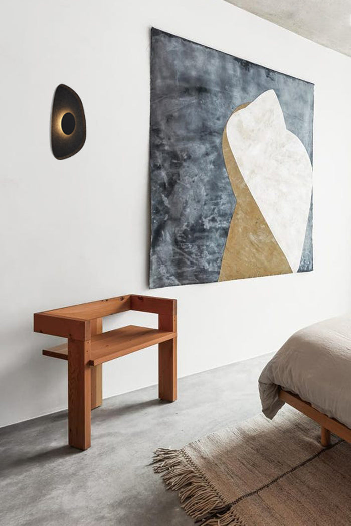 Black felt wall light installed in a bedroom over a chair.