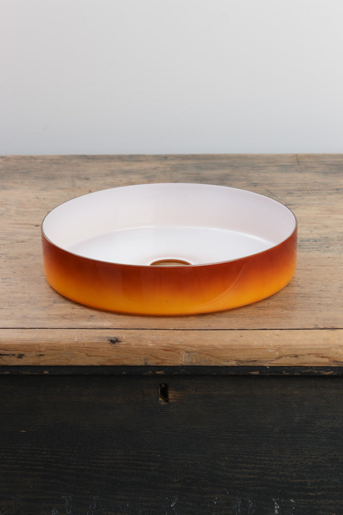 Amber circular shade with white inner, placed on a timber bench.