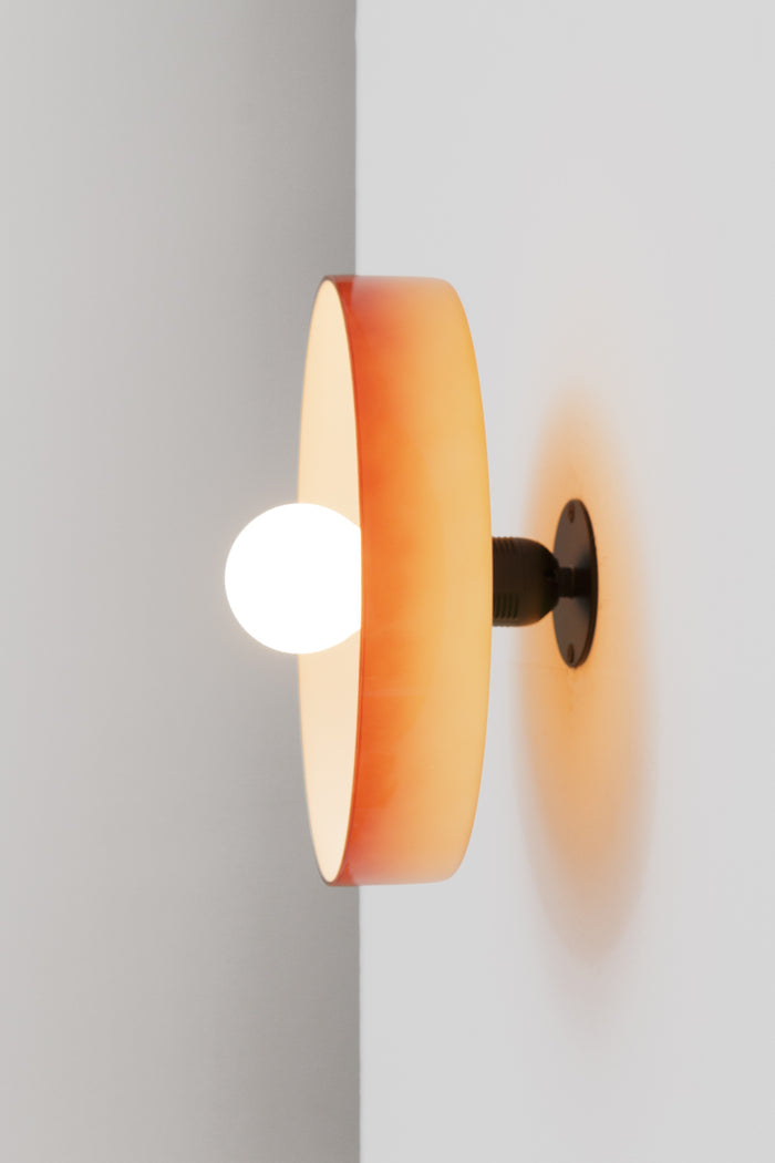 Wall mounted light with a curved rim, high-gloss finish and open shade work together to cast light outward with an effortless ambient glow