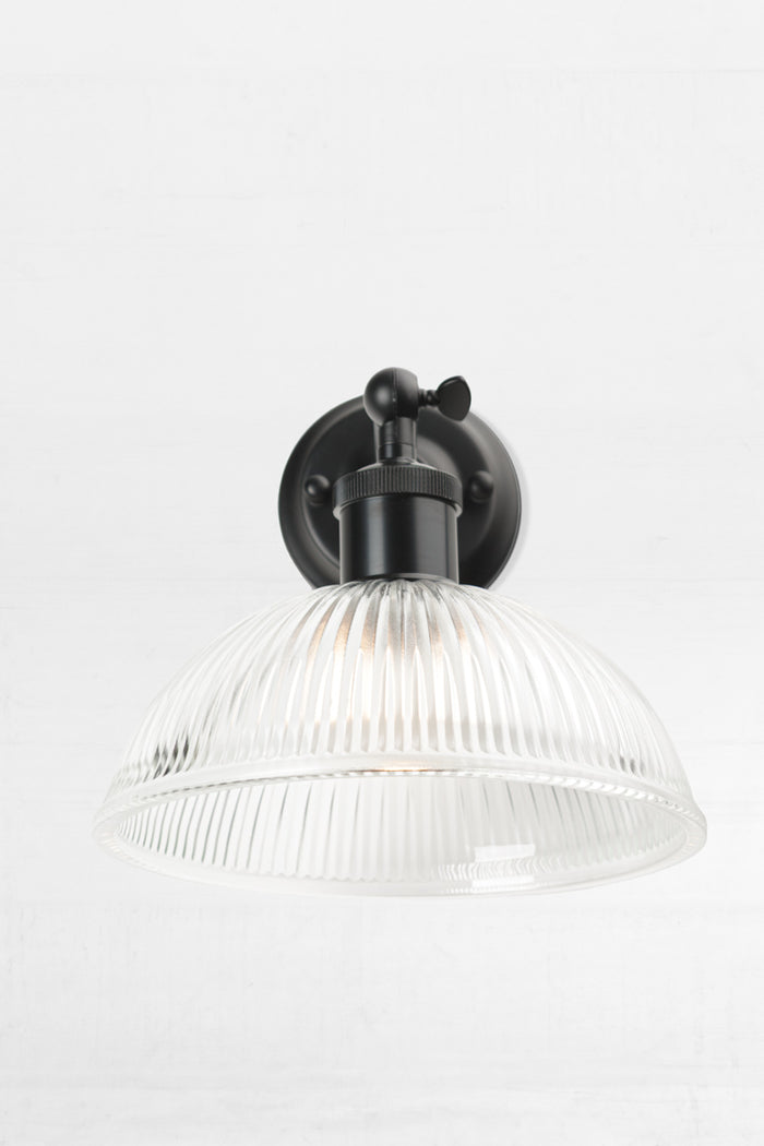 Small ribbed clear glass done shade on a short black straight arm wall scone, from the front.