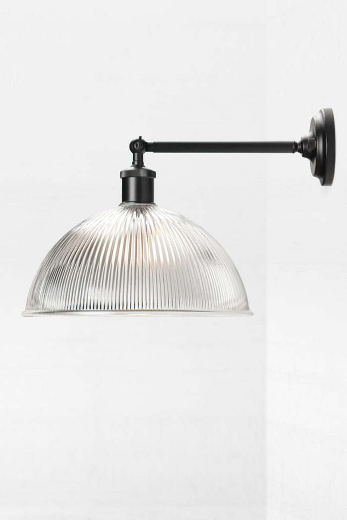 Medium ribbed clear glass done shade on a long black straight arm wall scone, from the side.