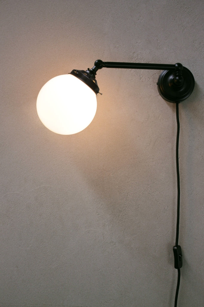 Opal glass ball shade on black adjustable wall sconce with wall plug.